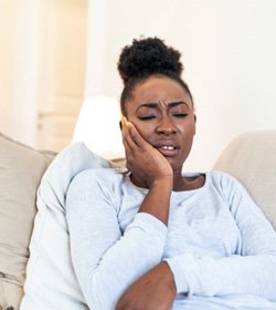 Woman sitting on sofa, experiencing toothache pain